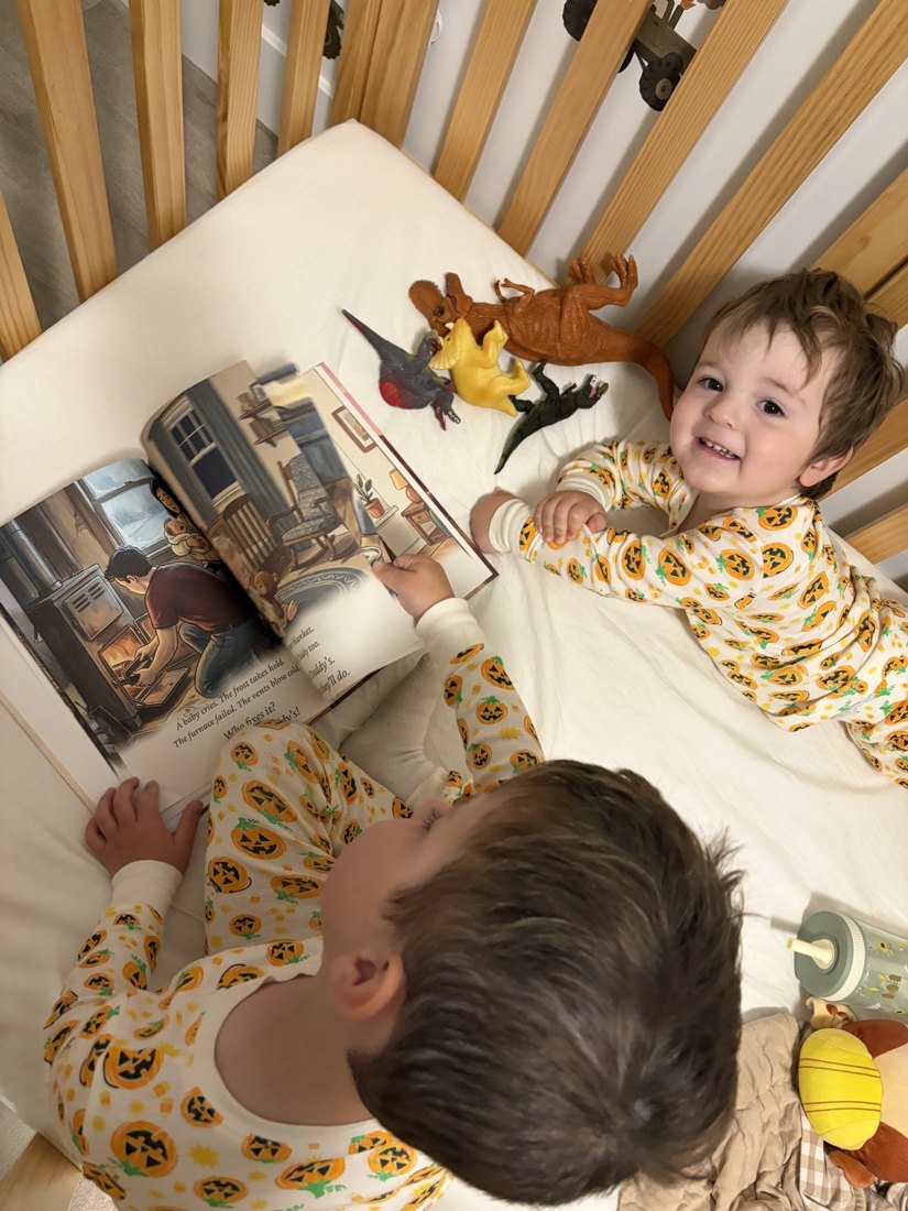 Two brothers in matching pajamas reading the book together in a crib